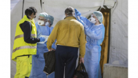 Three individuals in scrubs and masks, one of whom is scanning someone's tempreature.